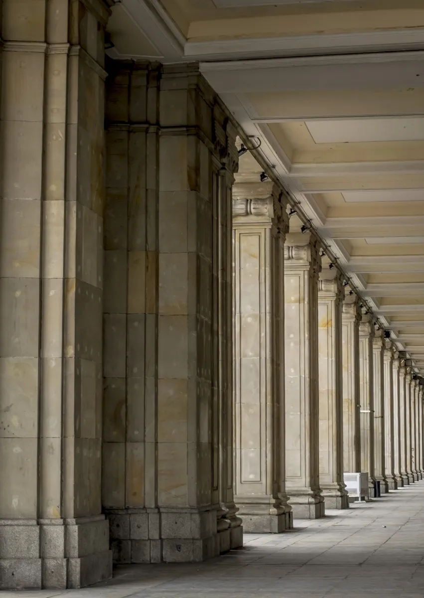 Long row of pale stone columns and ceiling bays receding through an empty arcade